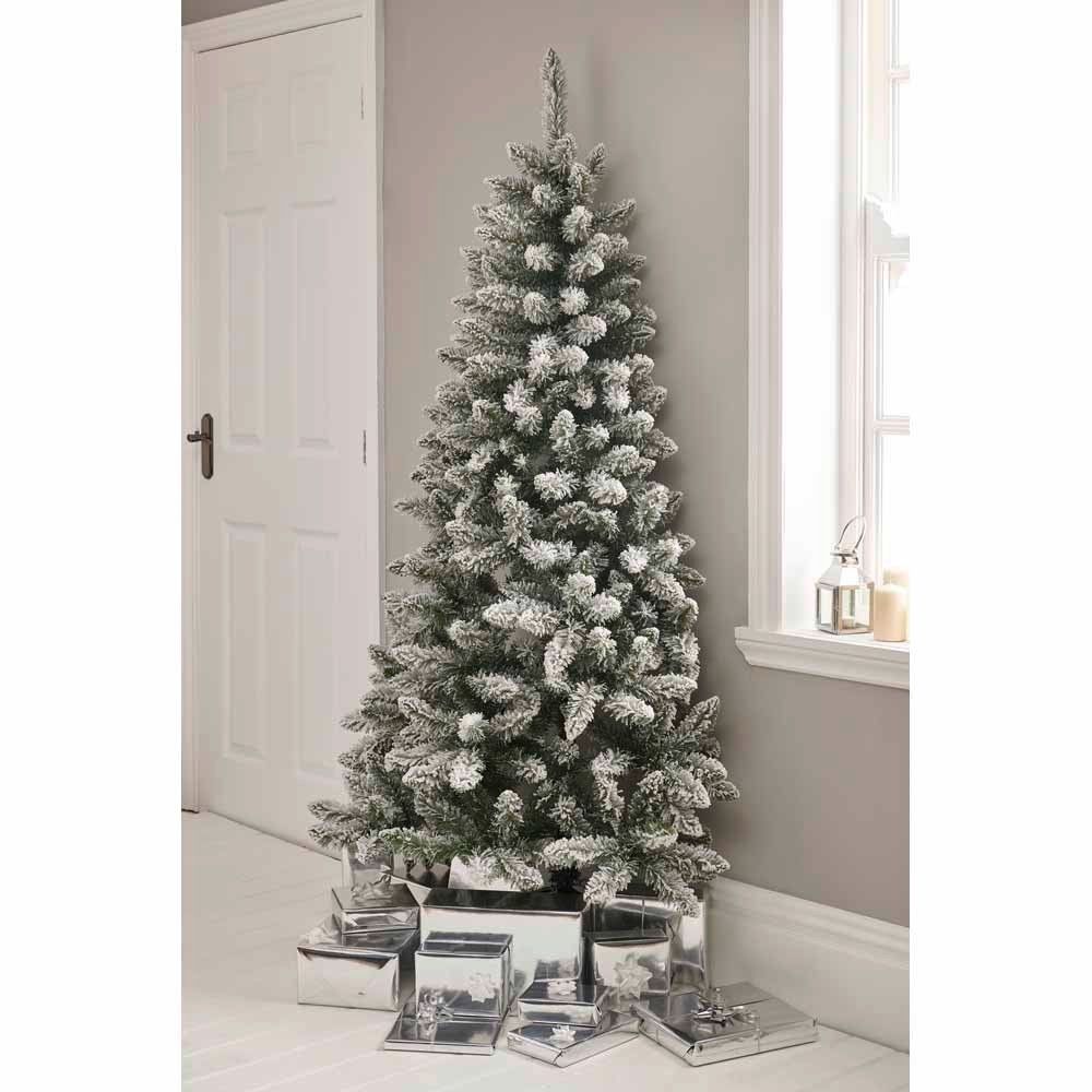 Wilko half flocked Christmas tree in a cosy living room surrounded by gifts wrapped shiny paper.