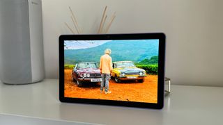 Amazon Fire HD 10 (2023) tablet on white shelf with man and two cars on screen