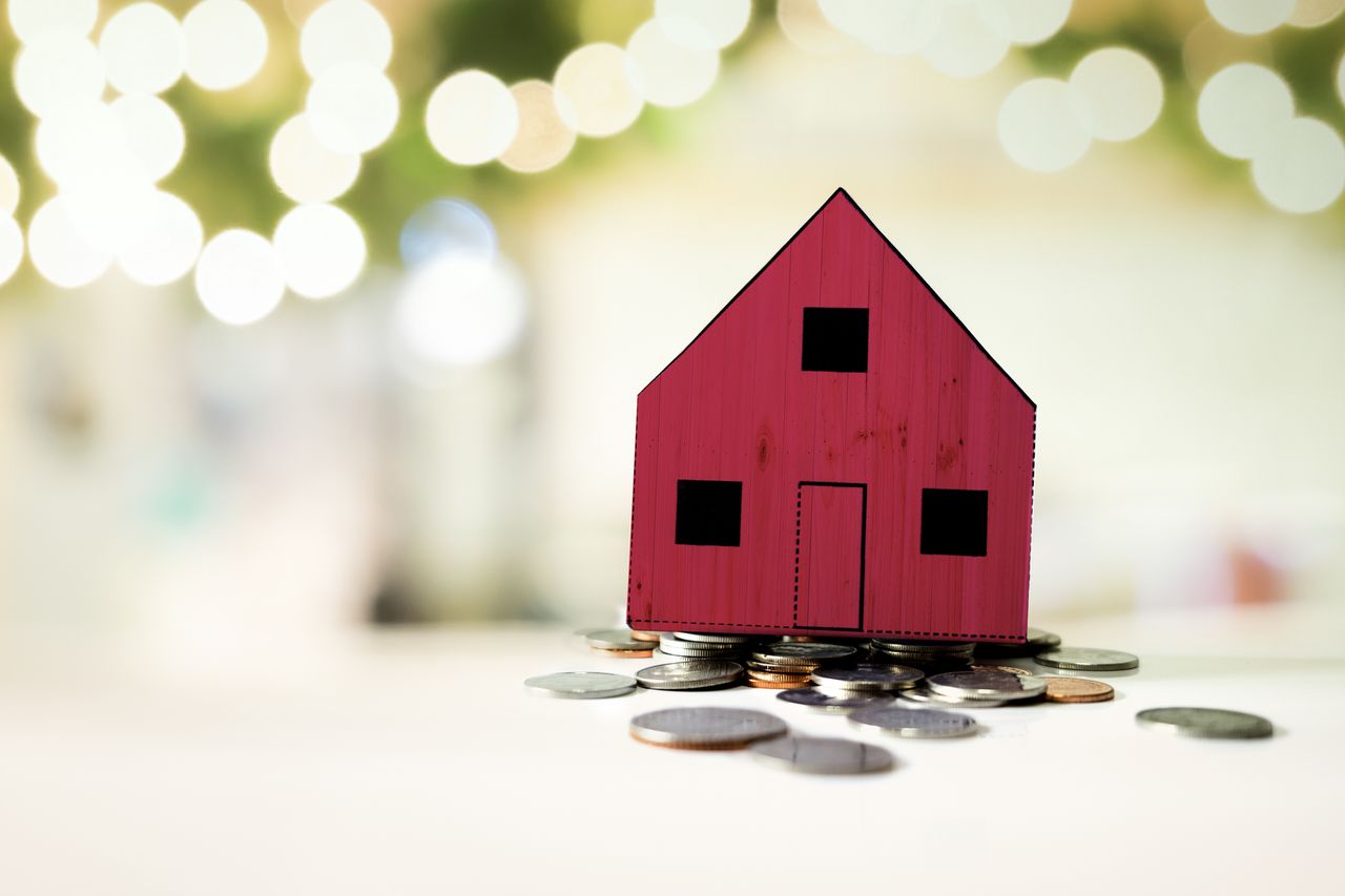 red house on pile of coins against a light background