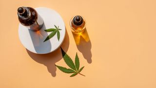 Lifestyle image of three vials of CBD oil with leaf on platform against yellow background