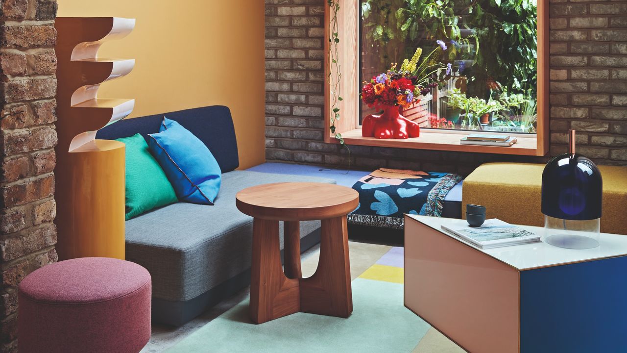 A mustard yellow-painted living room with colour-blocked furniture and a large window into the garden