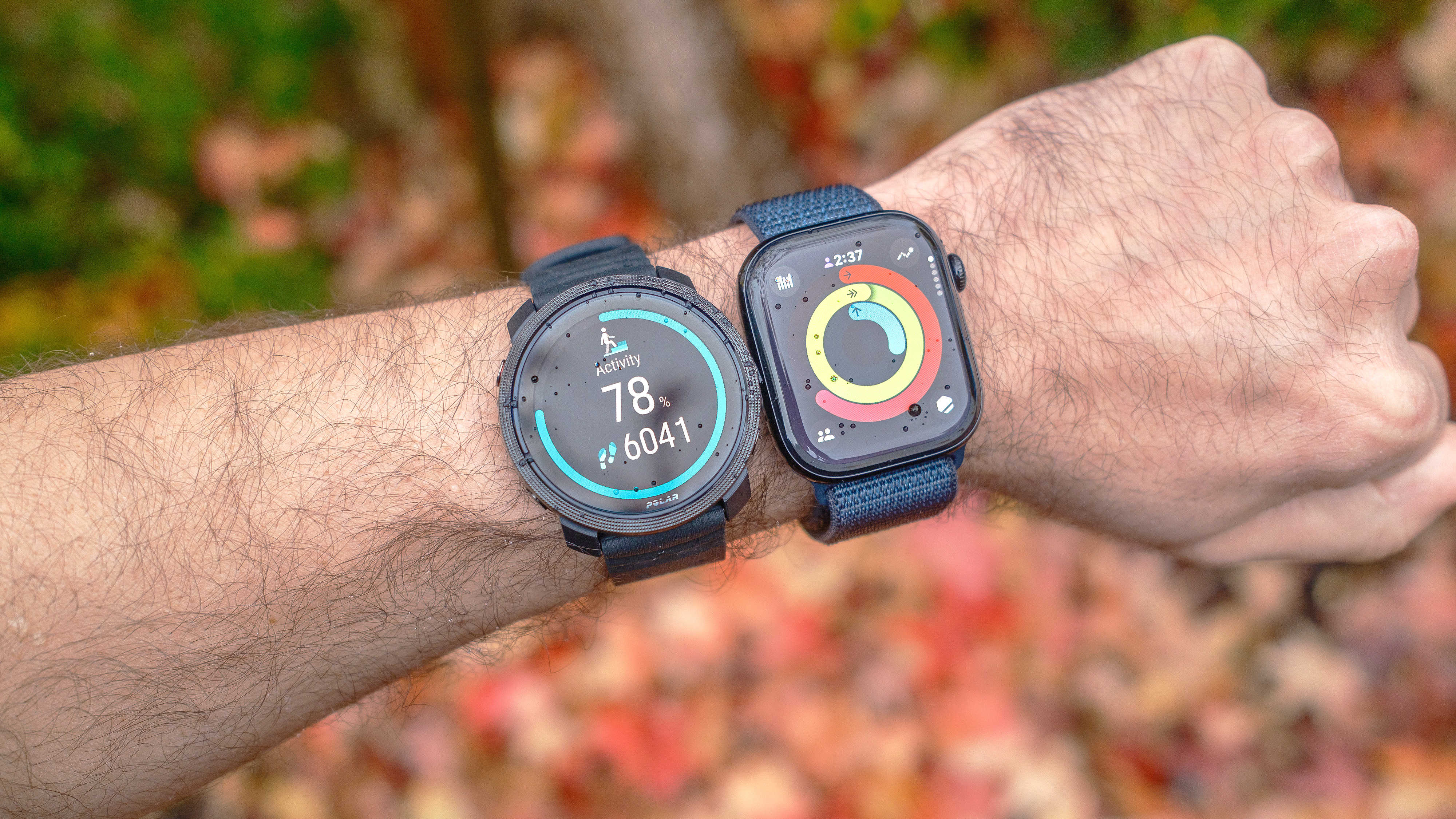 Close-up of the Polar Vantage M3 smartwatch next to the Apple Watch 10 on the user's wrist against a colorful background.