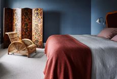 A small bedroom with deep blue walls and a red bed spread