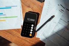A smart phone open to a calculator app, on tope of a few pieces of paper on a desk.