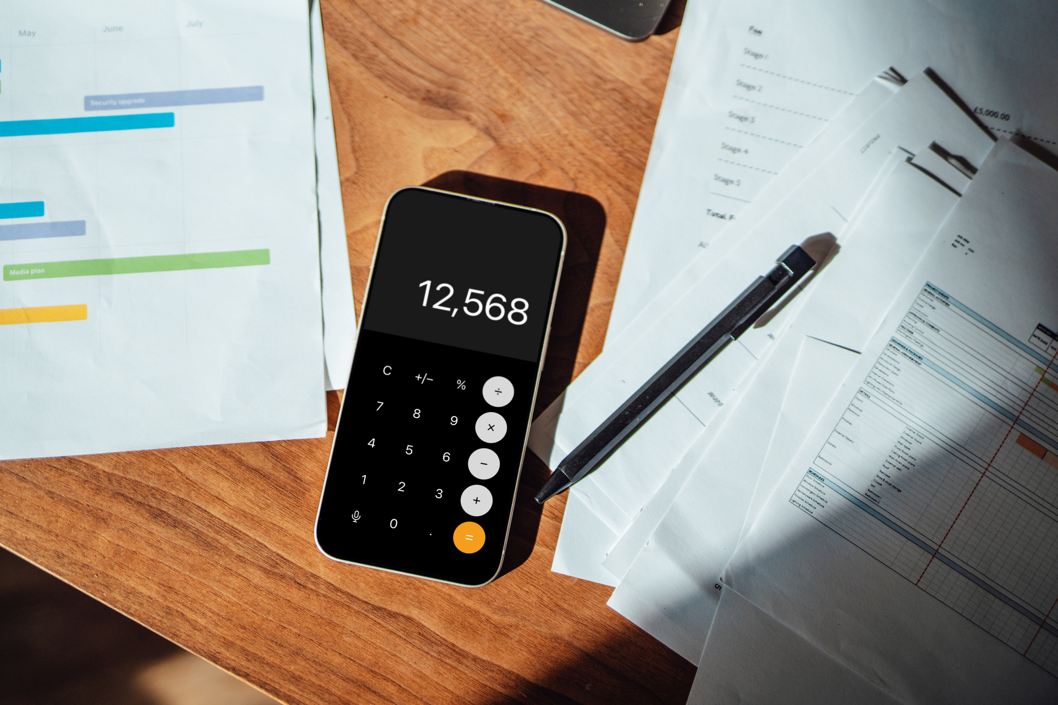 A smart phone open to a calculator app, on tope of a few pieces of paper on a desk.