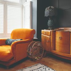 A black-painted living room with a mid-century sideboard, an orange armchair and a tasseled table lamp