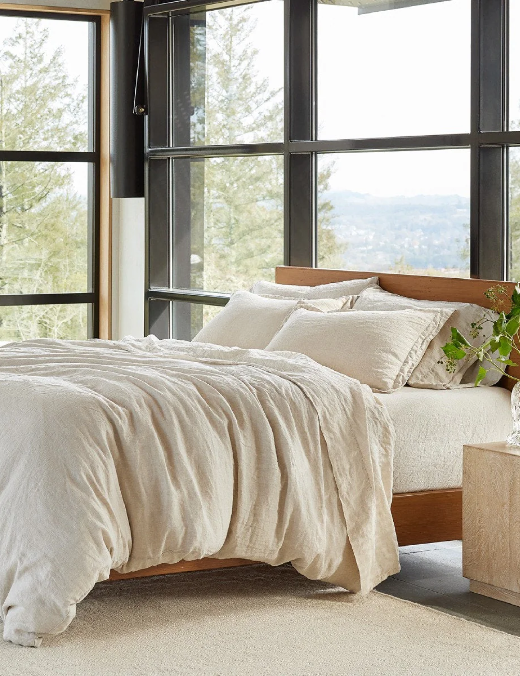 Neutral bedscape styled inside of a sunlit bedroom with floor-to-ceiling windowpanes