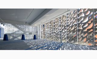 Interior view of the Leong Leong building, sunlight dances in through the screen's abstract apertures, grey concrete floor, white stairwell, blue cone shape stumps