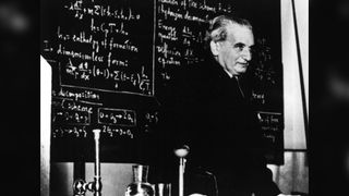 Theodore von Karman stands in front of a blackboard with equations.