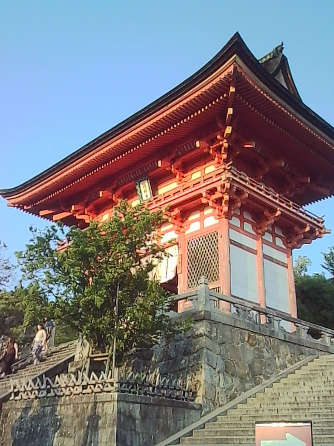 Red Japanese temple building glowing in warm sunlight beside stone steps.
