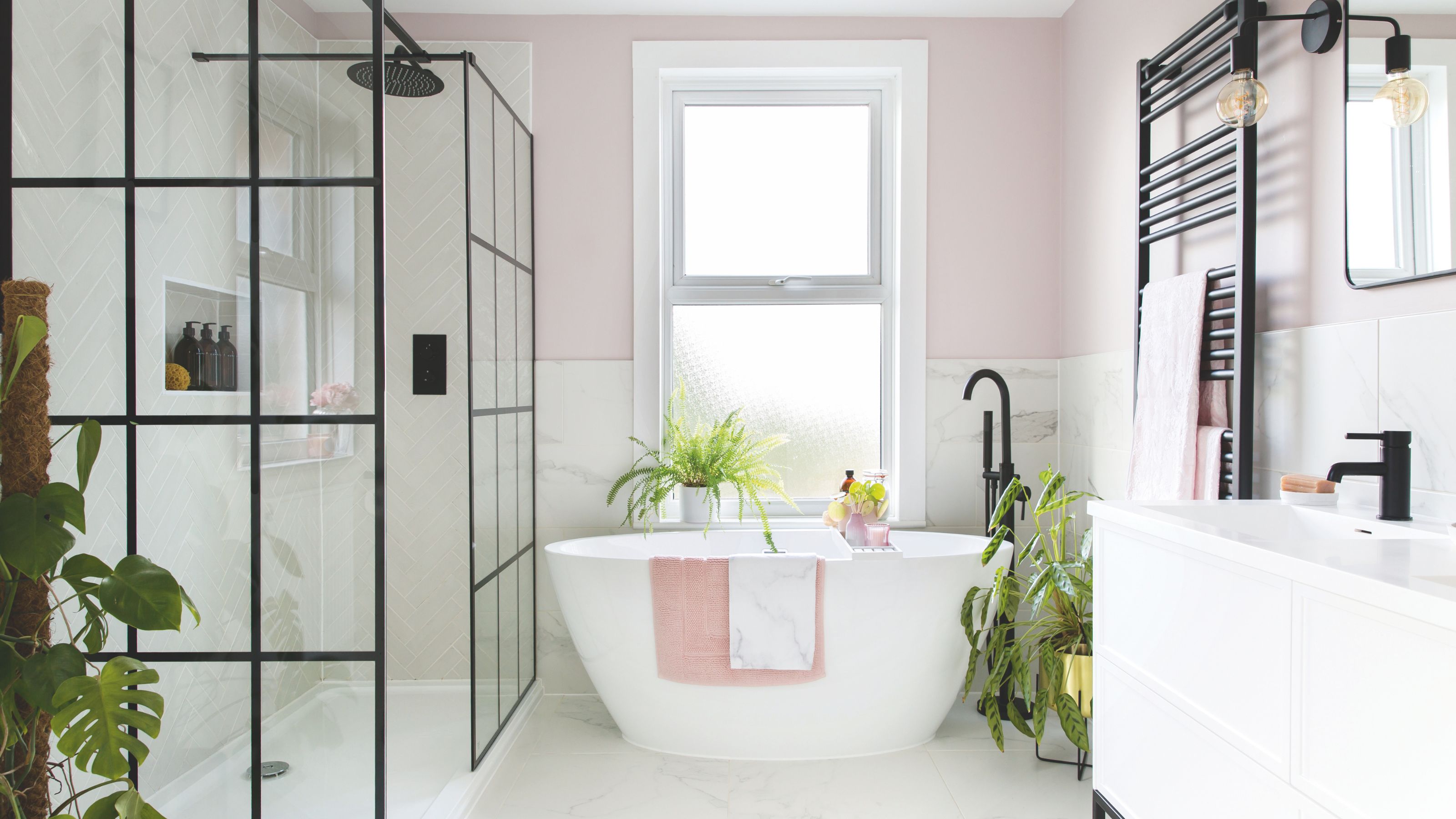 Pink painted bathroom with a freestanding bath in the middle, a shower area to the left and a sink on the right