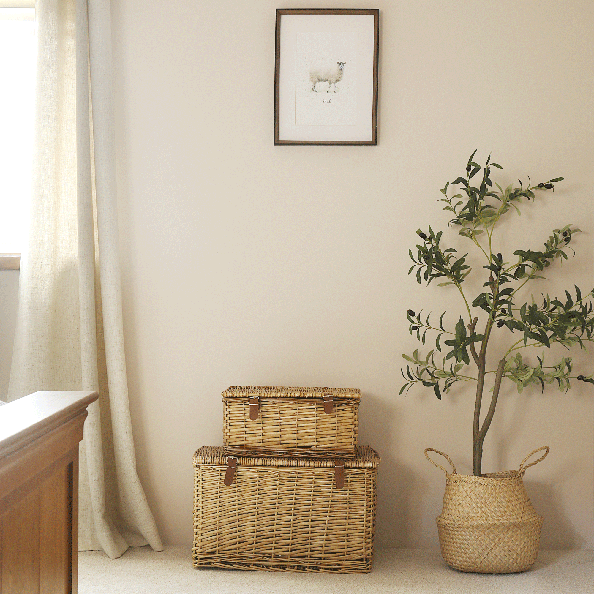 a corner of a bedroom with a decorative tree in a belly basket and a stack of wicker hampers beside it