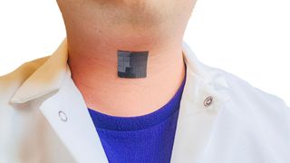 photo shows a shiny black patch made up of small squares stuck to a man&#039;s throat; he&#039;s wearing a white button down over a blue t shirt