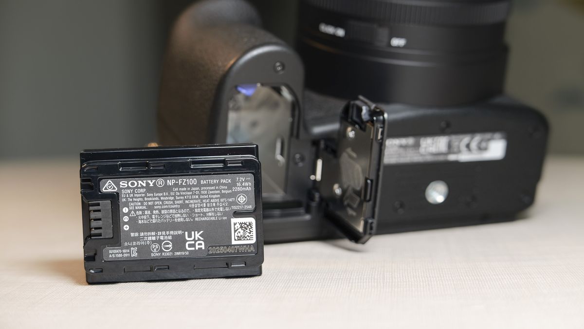Closeup of the Sony RX10 V bridge camera's battery door, and the battery has been removed and placed on the table in front of the camera
