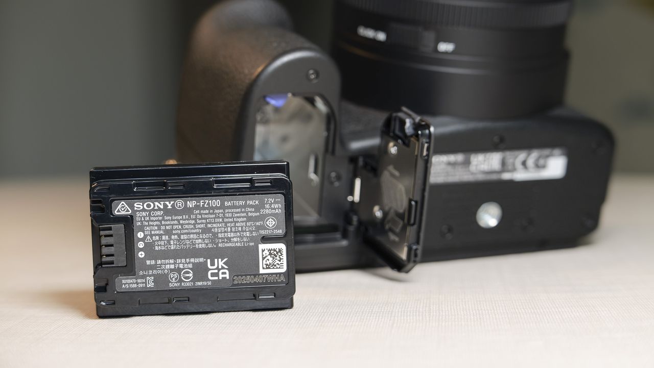 Closeup of the Sony RX10 V bridge camera's battery door, and the battery has been removed and placed on the table in front of the camera