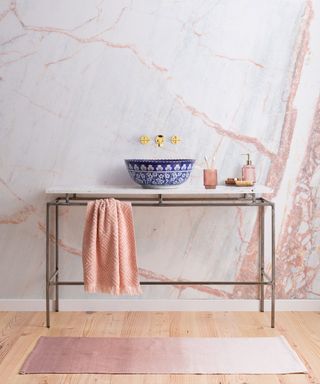 A decorative wash basin in a small bathroom with a marble-effect dusty pink wall