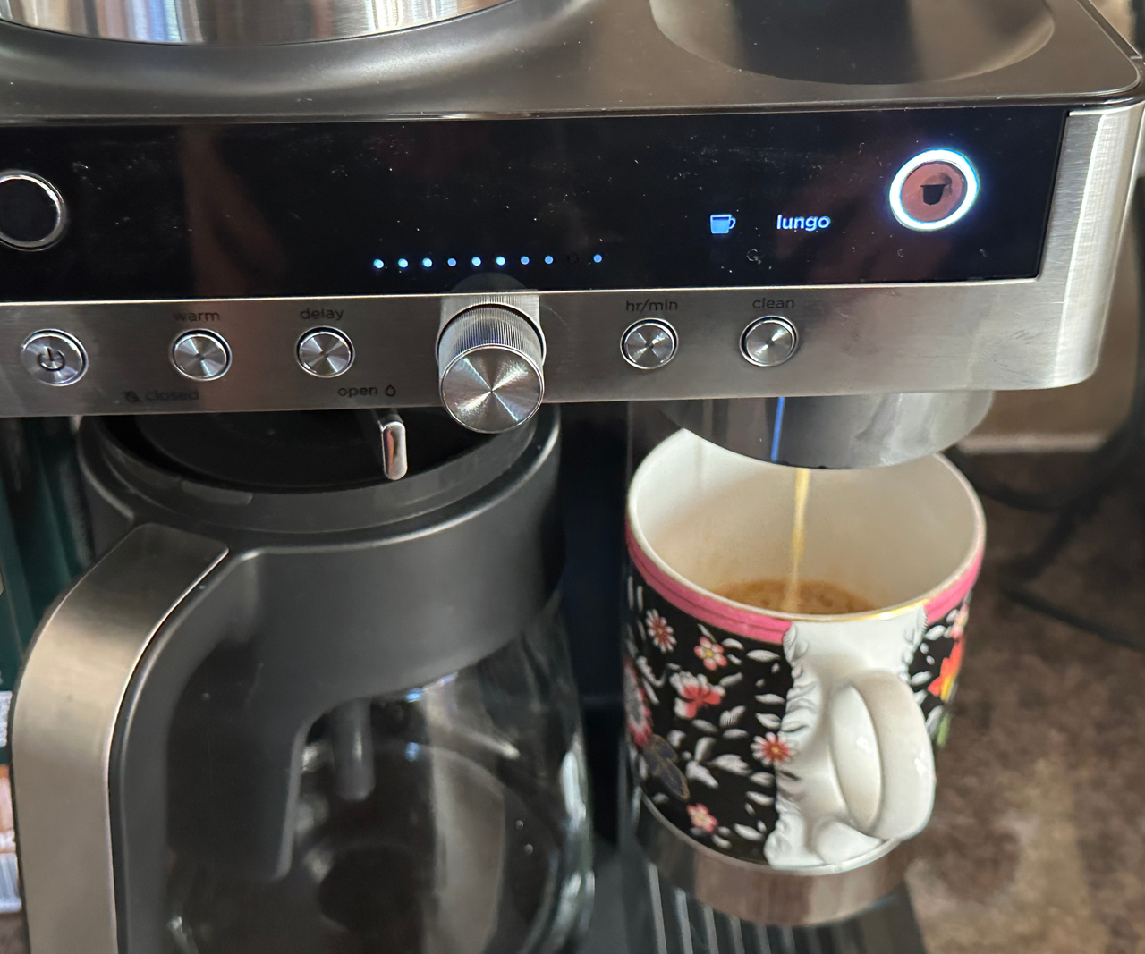 A close up of a coffee mug being filled with coffee from a pod beside a carafe on the drip coffee maker tray.