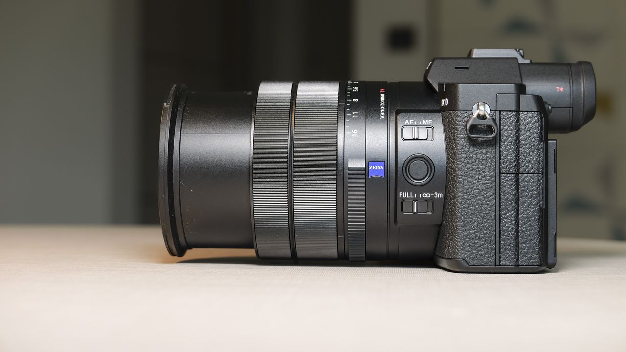 The side profile of the Sony RX10 V bridge camera, on a white table with a patterned wallpaper background, its lens is half retracted