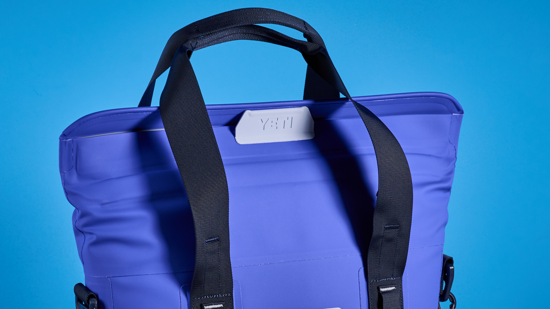the yeti hopper m15 cool bag with a padded carry strap, handles, and a 15 quart capacity photographed with coke zero cans against a blue background