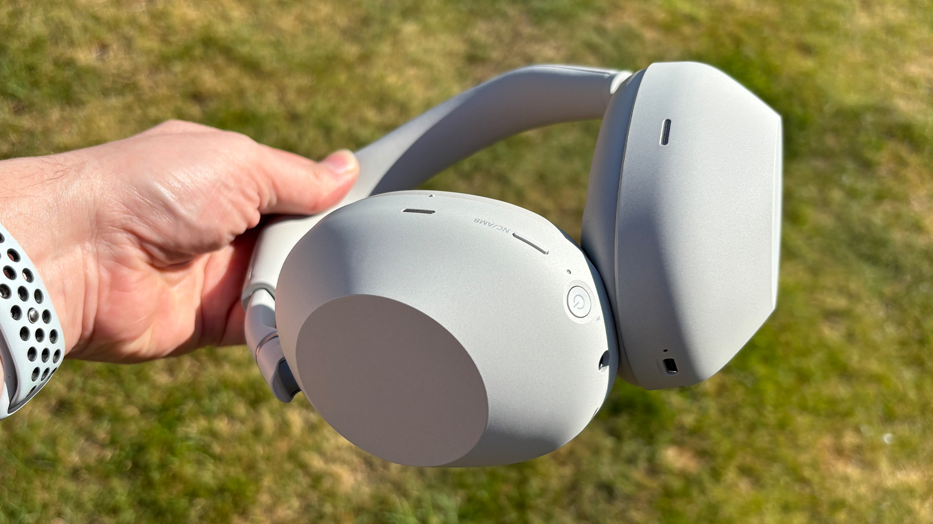 Sony WH-1000XM6 over-ear headphones held in hand above lawn