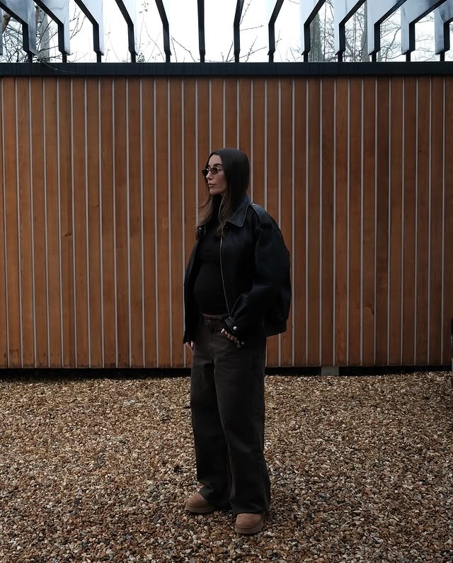 Millie wears a black bomber jacket, black jeans, and Ugg boots.