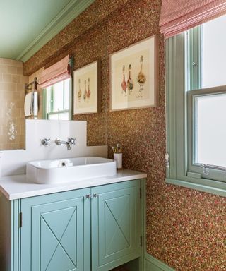 Bathroom with floral wallpaper and blue painted ceiling, cupboards and window frame