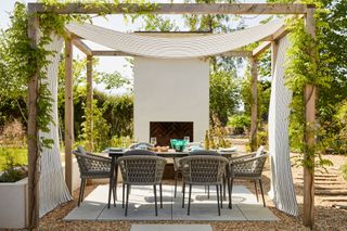 wooden pergola with draped fabric over outdoor dining area by Bridgman