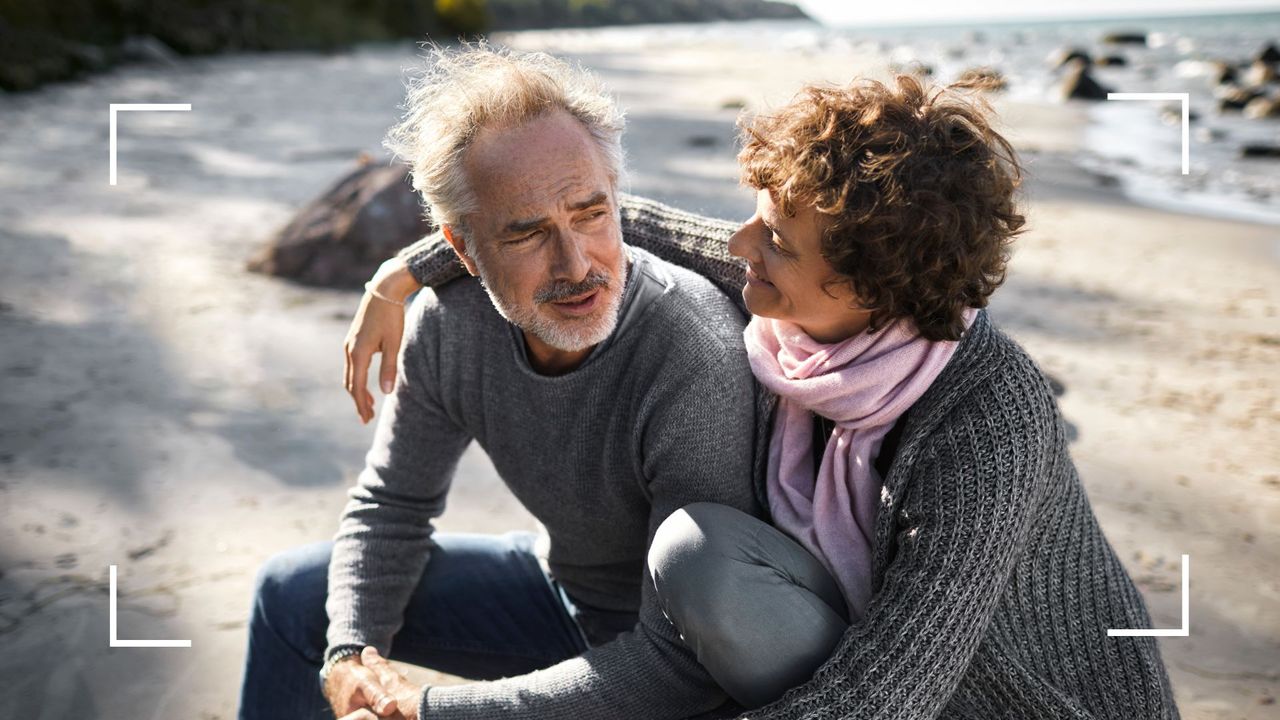 Man and woman sitting on a rock on the beach hugging, representing how to talk about expectations in a relationship