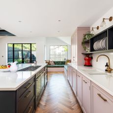 Kitchen island and pink cabinets with white countertop in front of bay windows