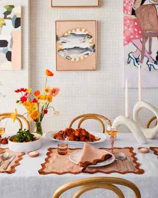 A festive dining table features terracotta-hued tableware, sculptural candleholders, and drinks and food.