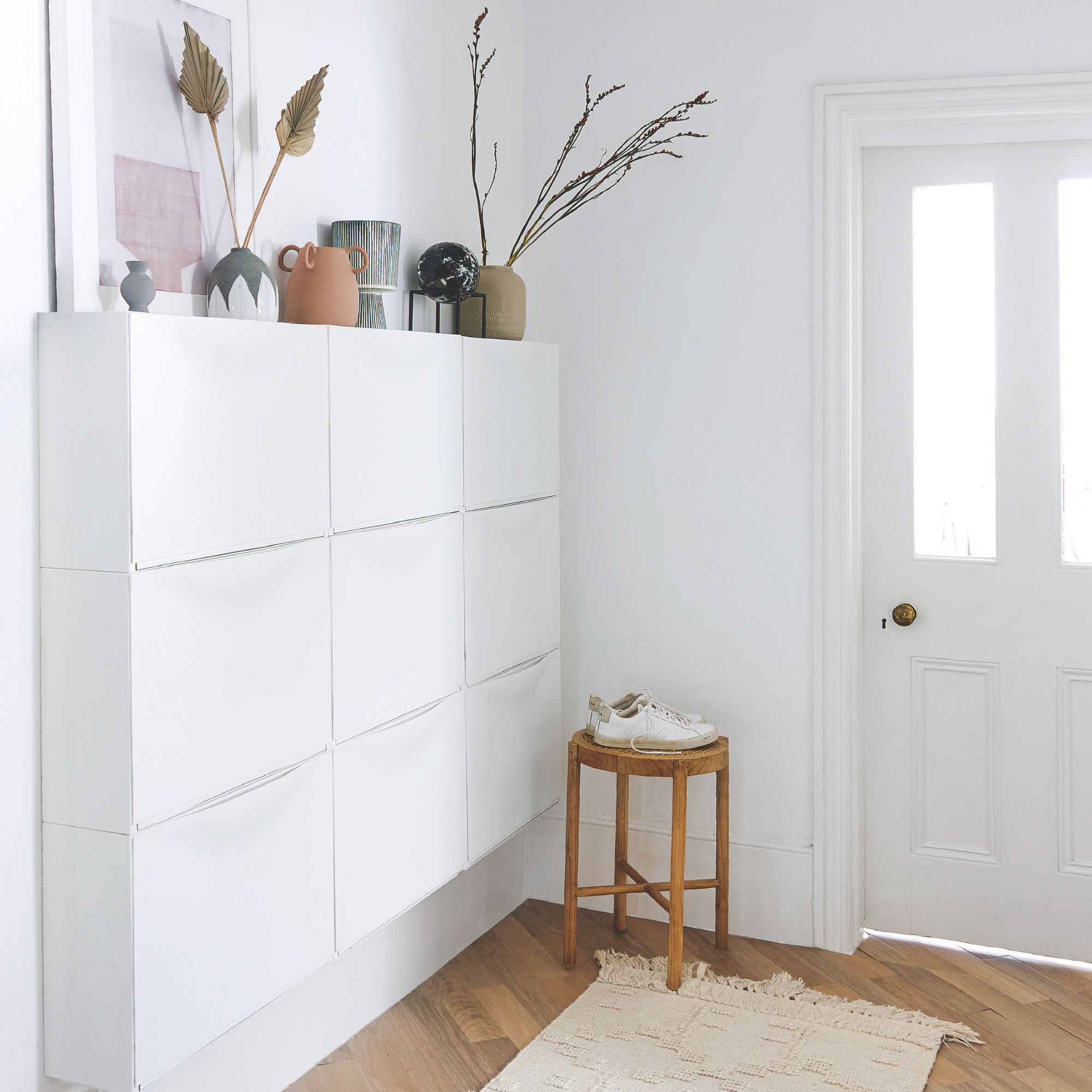 White painted hallway with white shoe storage cabinets on the wall, a stool by the door and a rug on the wooden floor