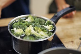 Raw broccoli being cooked in a pan of water on the hob