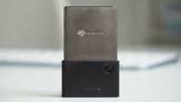 Xbox Series X|S Seagate Storage Expansion Card on a white surface, partially inserted into a black adapter featuring the Xbox logo, blurred background.