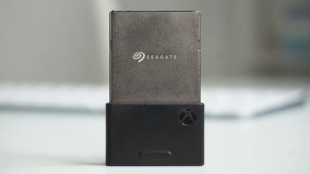 Xbox Series X|S Seagate Storage Expansion Card on a white surface, partially inserted into a black adapter featuring the Xbox logo, blurred background.