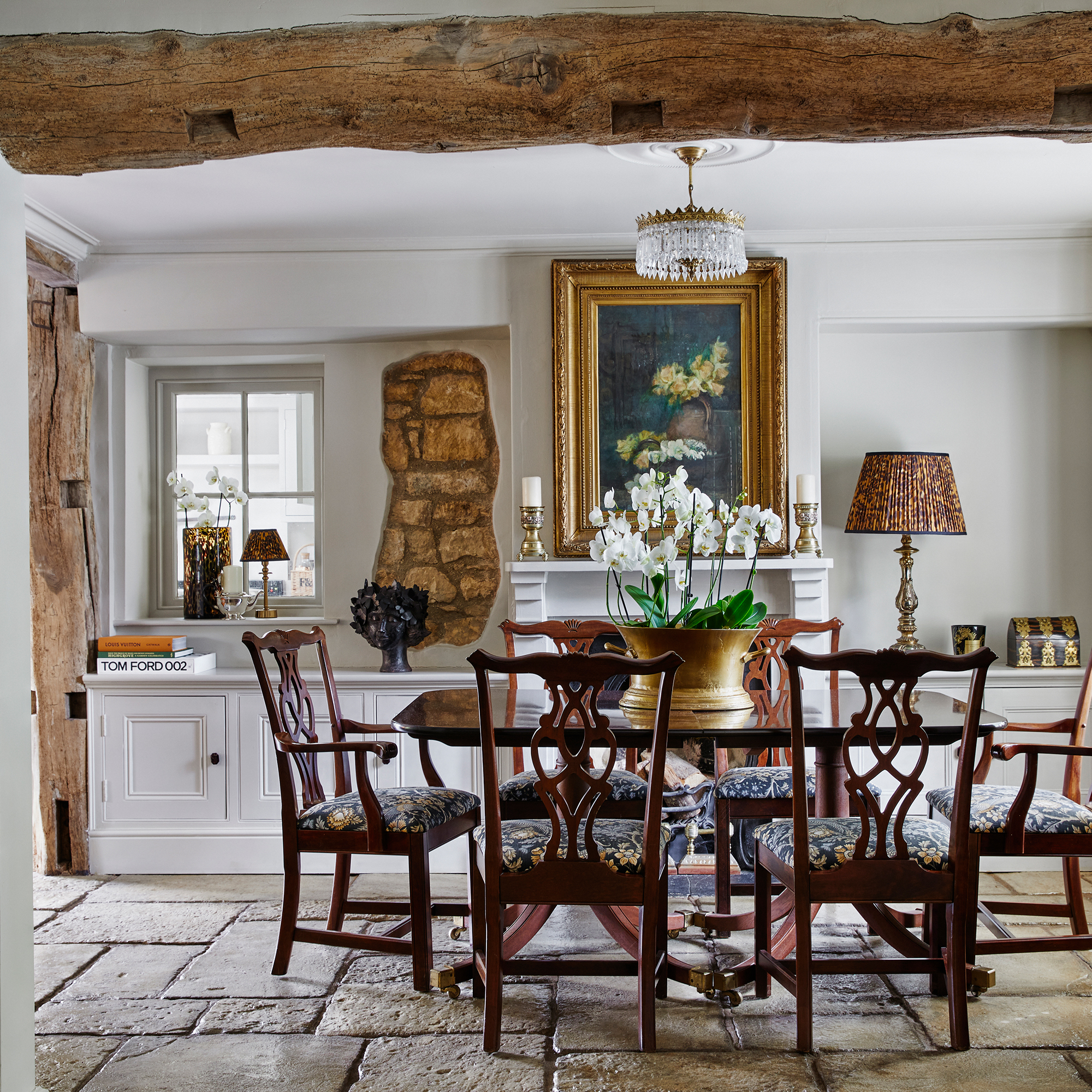 Country style dining room with wooden ceiling beam, dark wood dining table and chairs, flagstone floor and exposed cotswold stone on wall