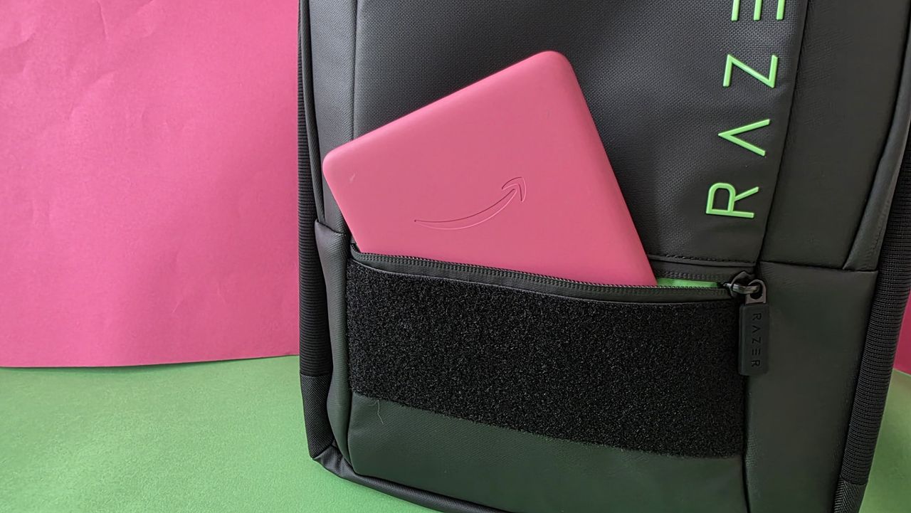 A black Razer backpack with the front pocket open and pink Kindle placed inside