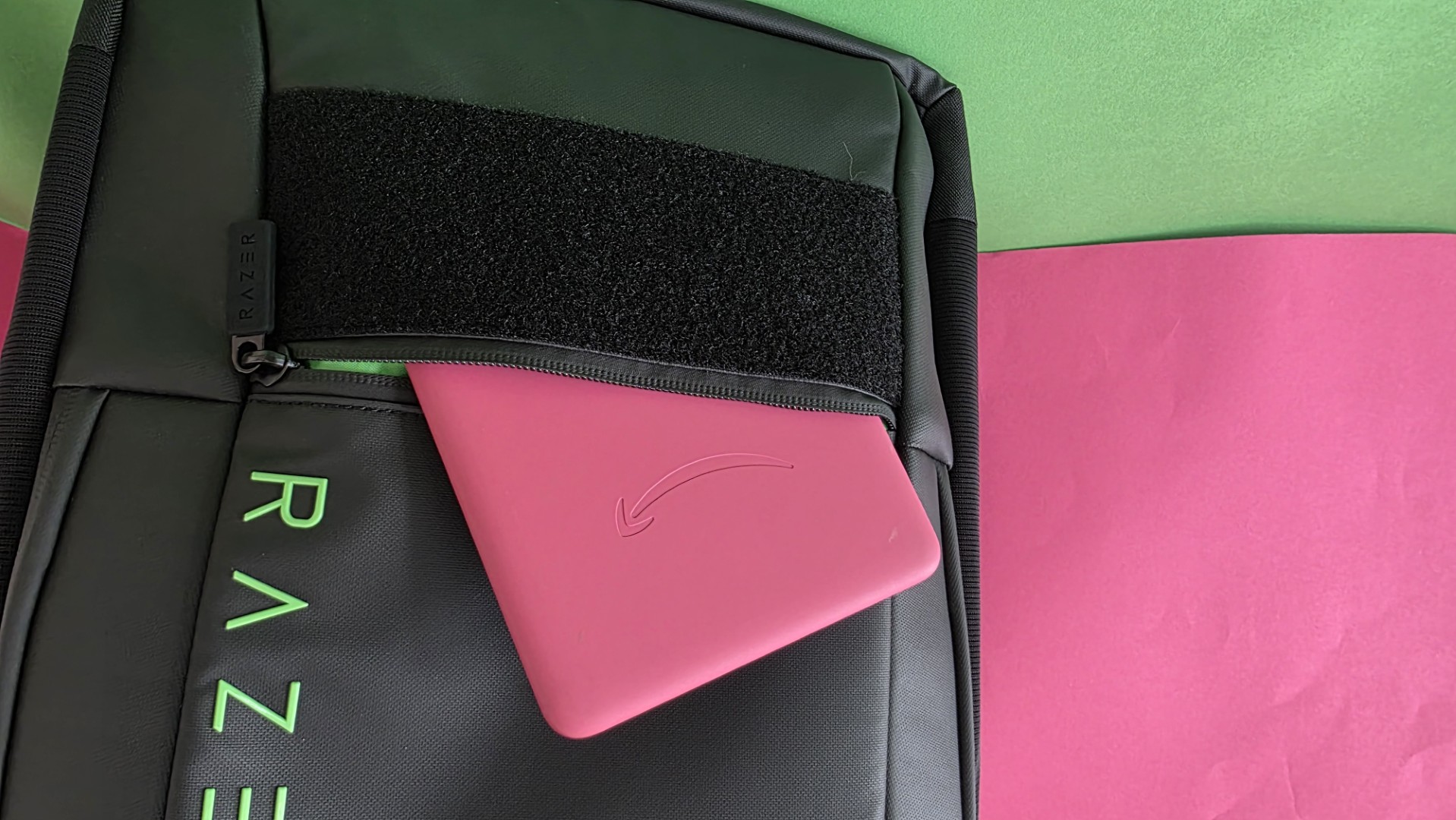 A black Razer backpack with the front pocket open and pink Kindle placed inside
