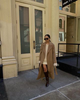 Autumn Boot Trends 2024: Influencer wears pointed-toe knee boots with a cream dress and a camel coat