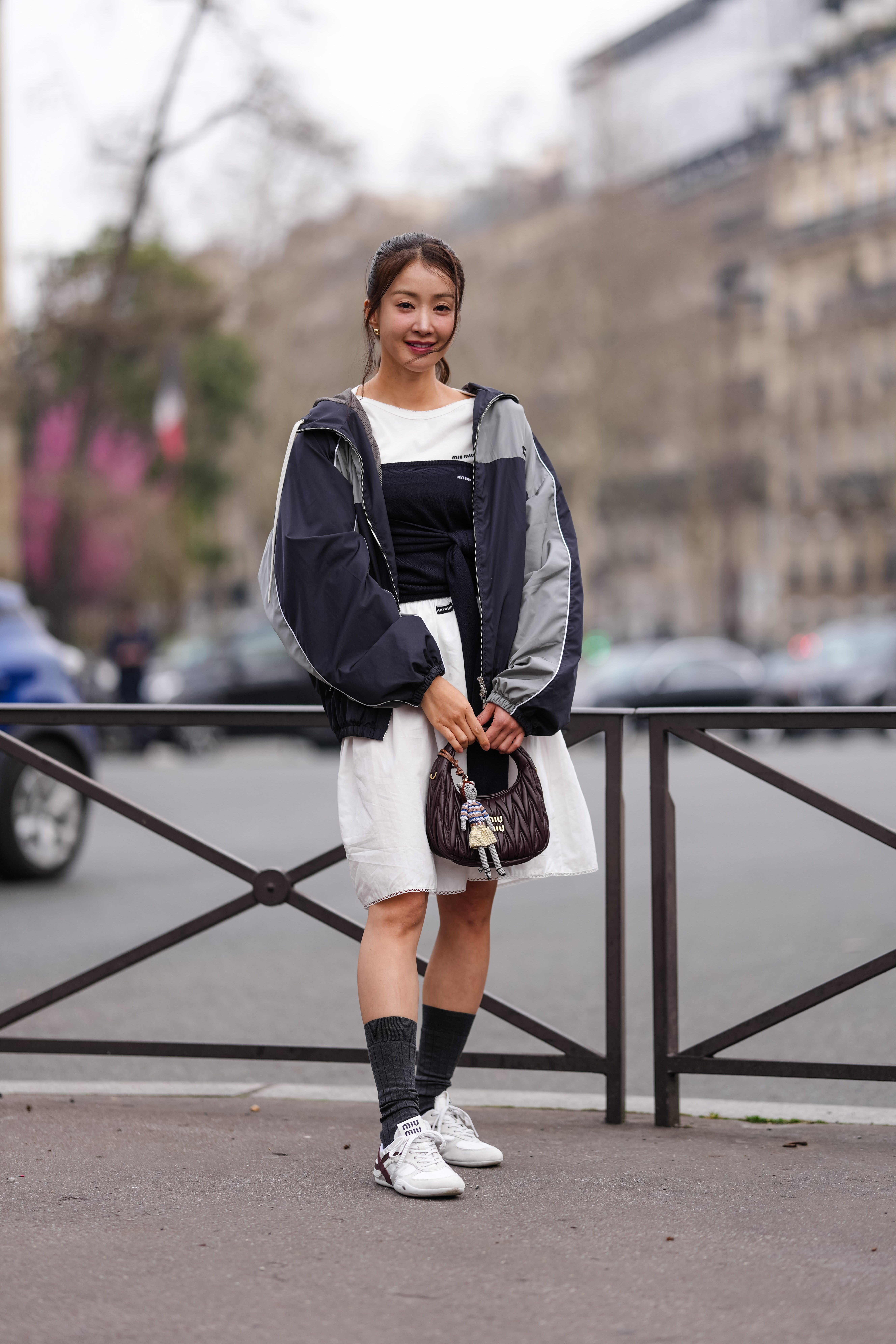 PARIS, FRANCE - MARCH 11: Lee Si Young wears gold earrings, white Miu Miu shirt, black strapless knit Miu Miu top, light gray black oversized Miu Miu jacket, white high waisted Miu Miu over the knee skirt, shiny dark brown Miu Miu Matelassé leather bag, bag charm, dark gray socks, outside Miu Miu, white Miu MIu sneaker shoes, during the Paris Fashion week Women's Fall/Winter 2025-2026 on March 11, 2025 in Paris, France. (Photo by Edward Berthelot/Getty Images)
