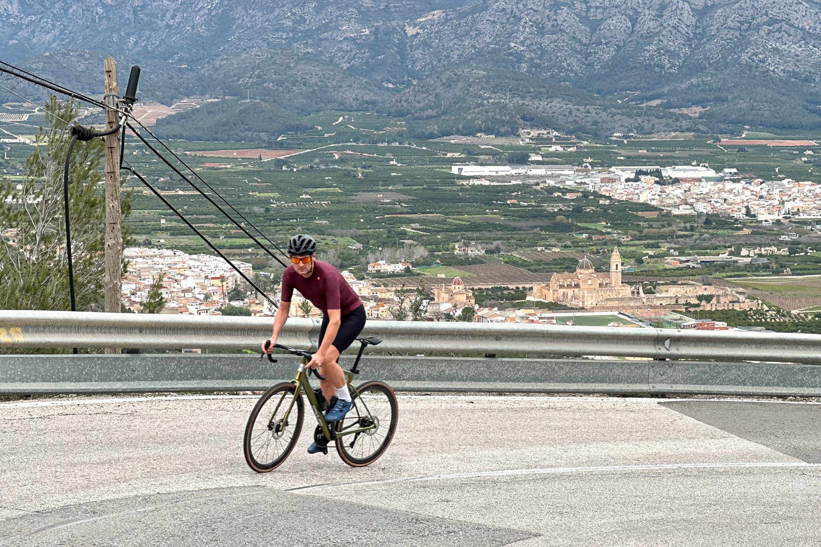 Man riding a bike up a hill in Spain wearing a purple jersey and a black helmet