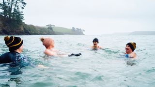 Group of people cold water swimming wearing woolly hats in a lake in Cornwall