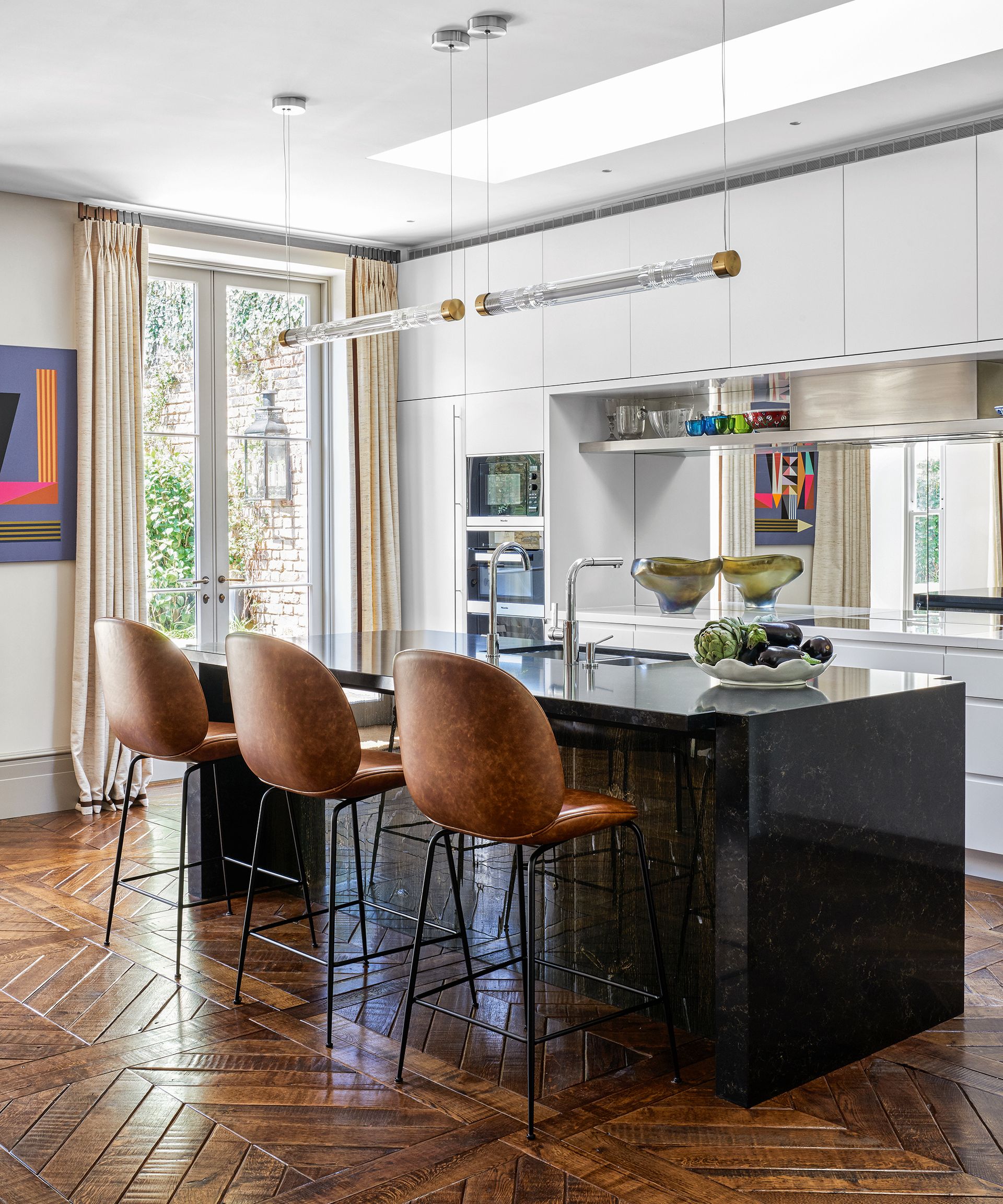 An example of how much does a new kitchen cost showing a white kitchen with a black island and upholstered bar stools