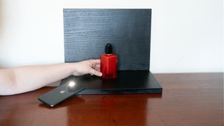 A person setting the scene by positioning a red perfume in front and on top of a black ground