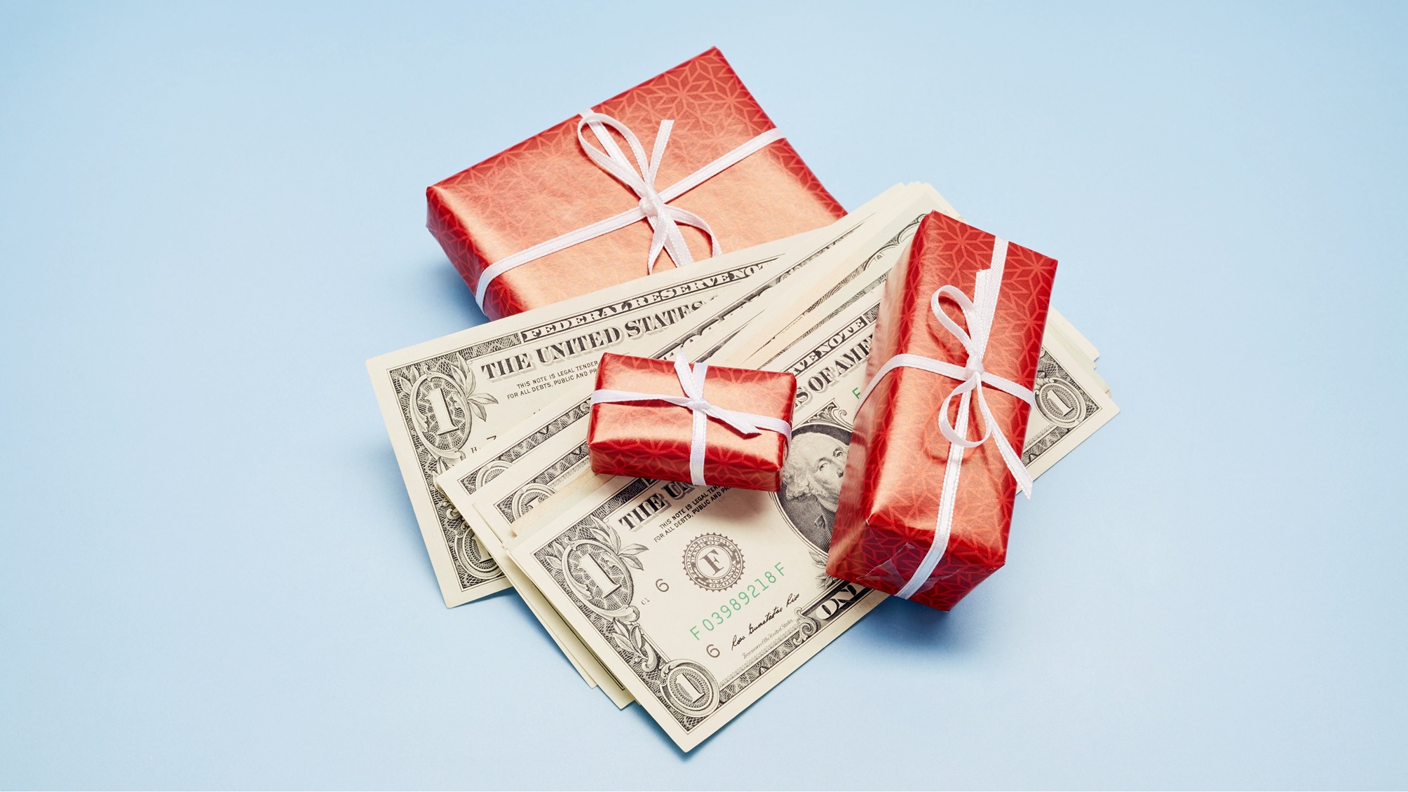 Small boxes wrapped in red with white bows and mixed in with dollar bills.