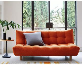 An orange three-seater sofa bed with quilted upholstery