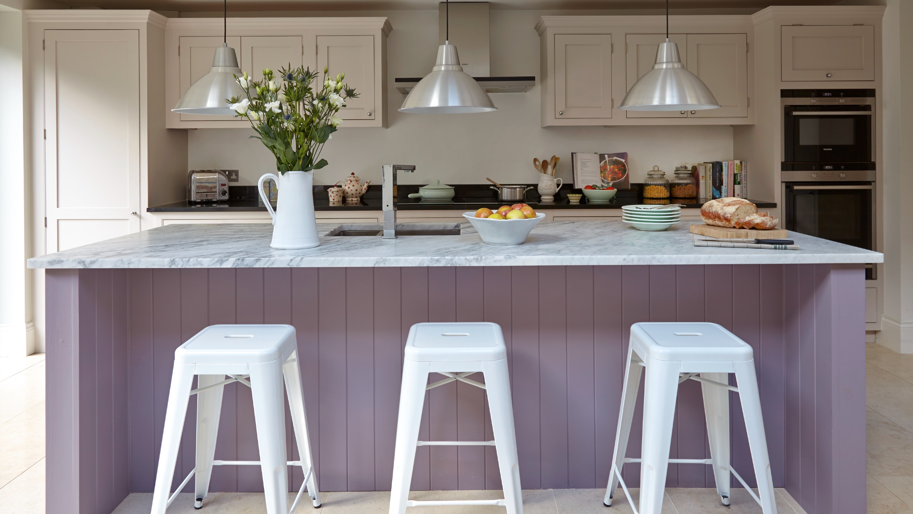A kitchen with warm off-white painted cabinets and a panelled kitchen island painted in lilac