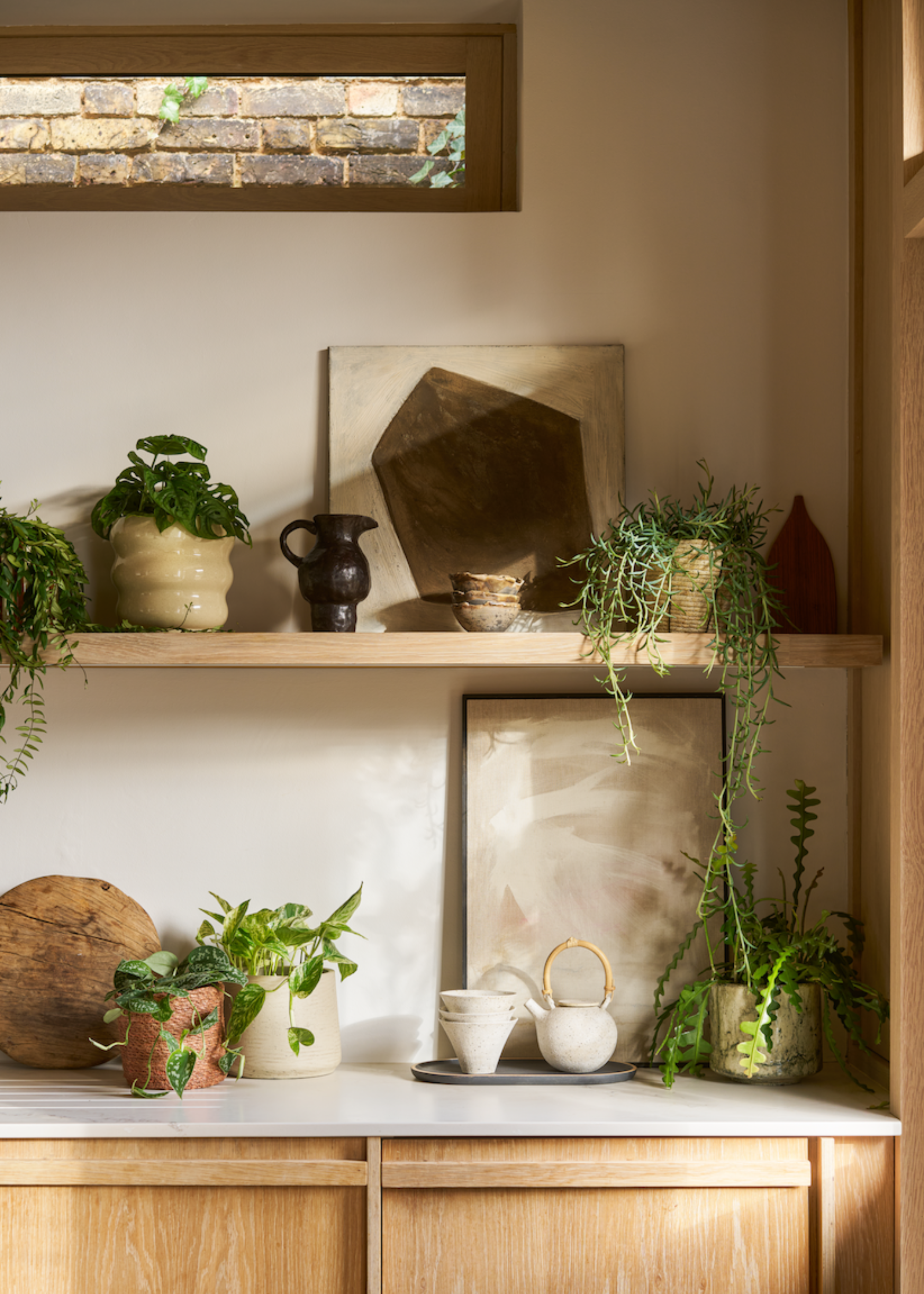 A kitchen corner with tea cups and a ceramic kettle by trailing plants