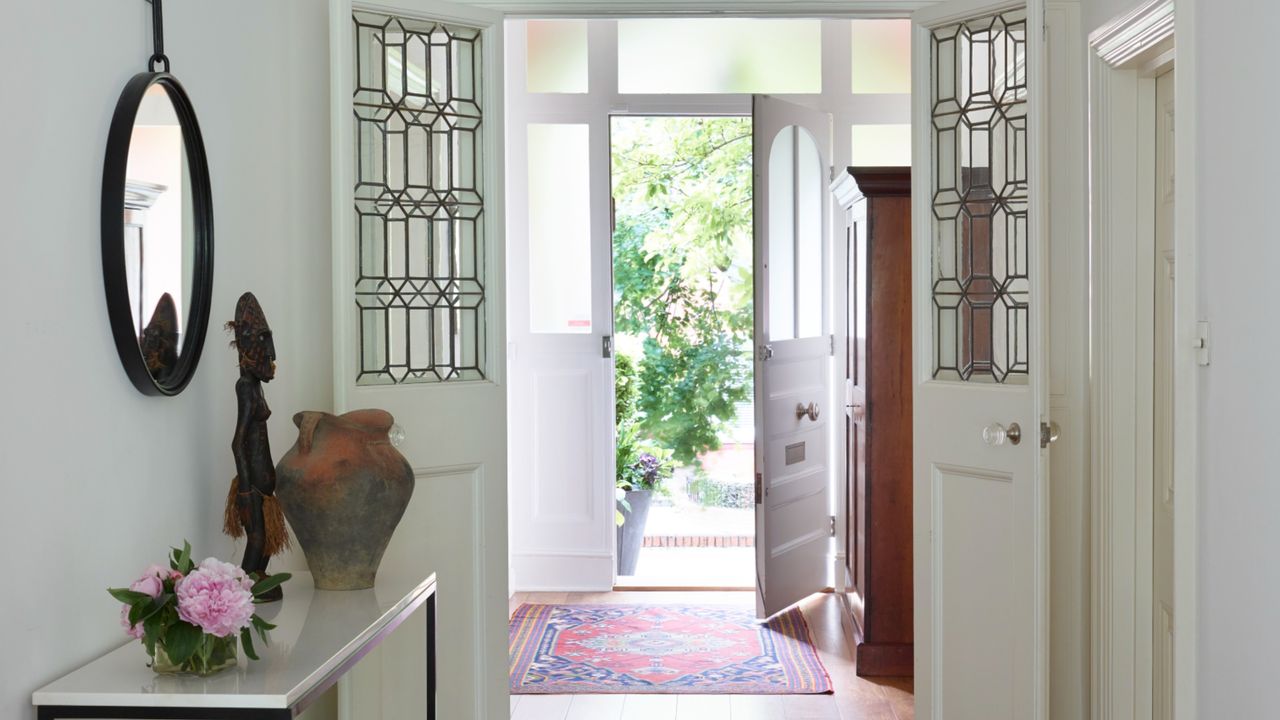 an all-white hallway with an open front door, and a side table, and mirror on the wall