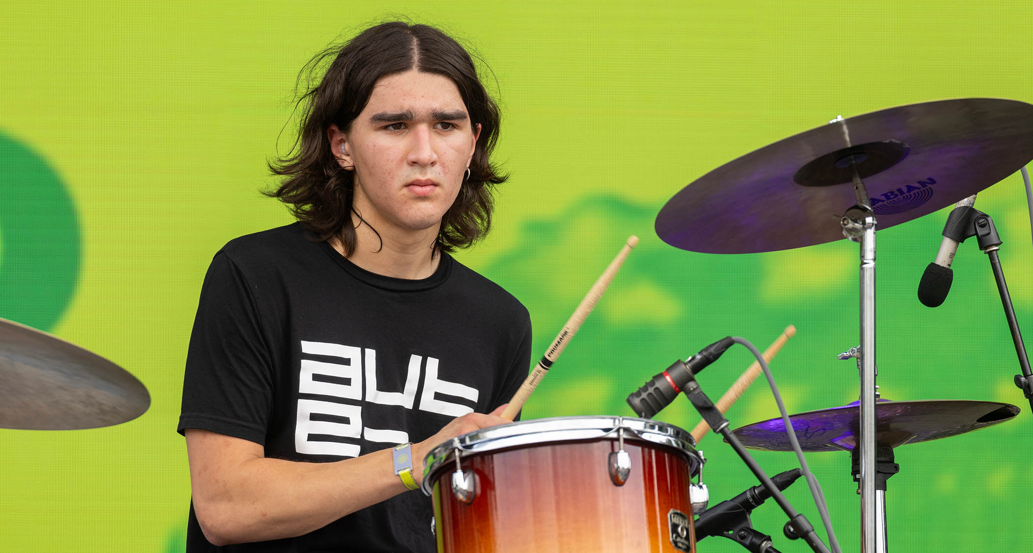Isaac Lowenstein of Chicago post-punk band Lifeguard plays drums against a green backdrop.