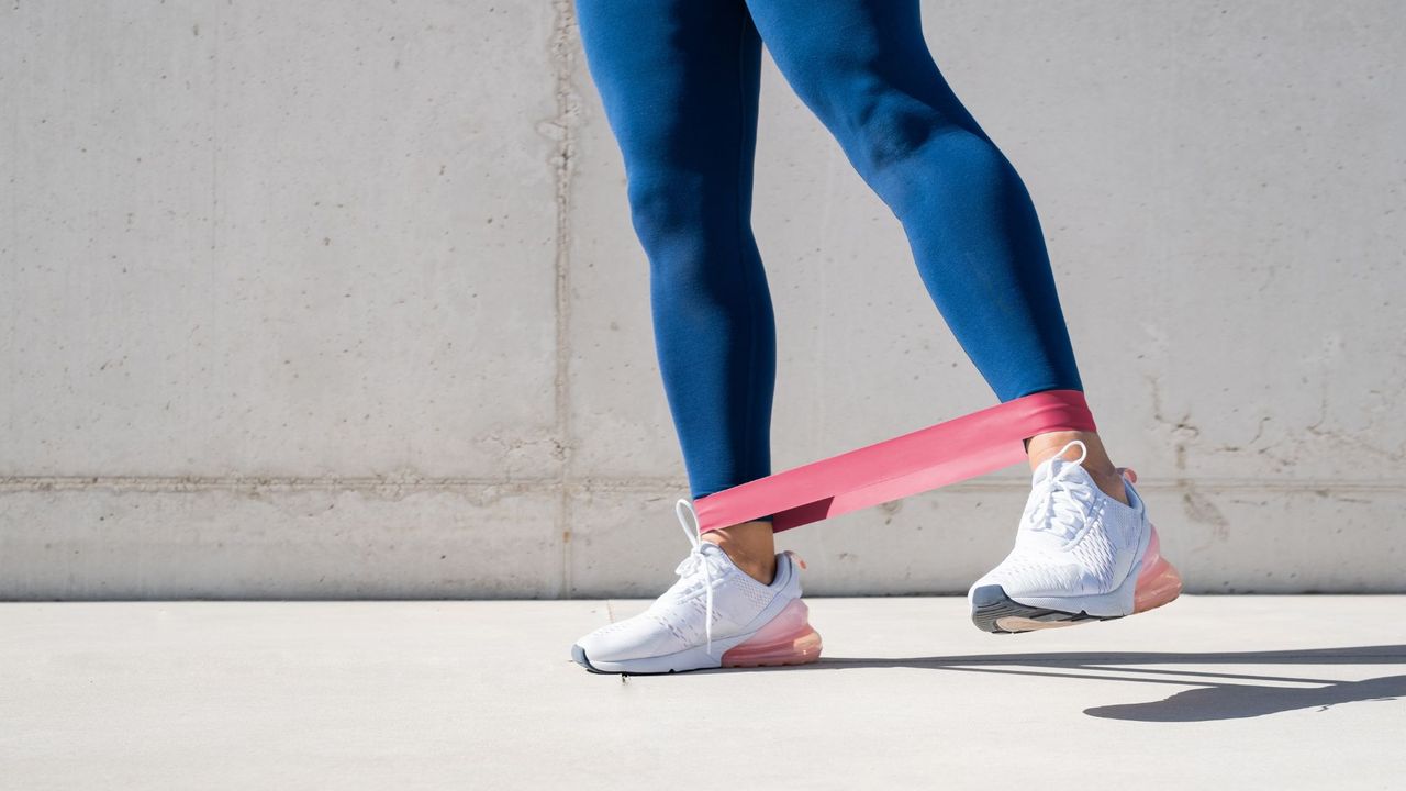 A woman doing a YouTube resistance band workout in the park